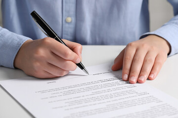 Woman signing document at white table, closeup