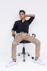 A poised young Filipino man is seated comfortably in an office chair against a white background, exuding confidence.