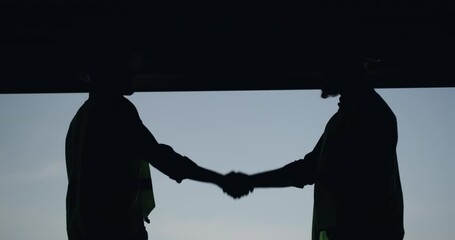 Construction, people and shaking hands on deal in partnership with door in garage or warehouse. Silhouette, men and handshake for commitment on project with contractor and engineer closing a site - Powered by Adobe