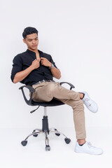 A poised young Filipino man dressed in smart casual clothes seated on an office chair, isolated on...