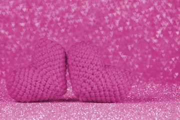 Two knitted pink heart on shiny pink backdrop. Heart shaped bokeh on background. Special day concept idea. Selective focus. Abstract background. 