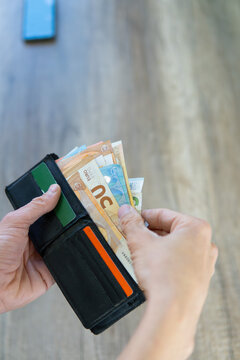 photograph of hands removing euro banknotes from a wallet with cards. phone on the table