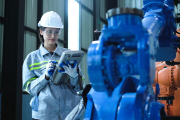 Female factory engineer using handheld robot control panel to check the operation of industrial robot arm and upgrading new software programming.