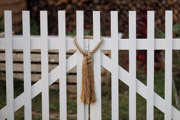 A beige rope knot hangs on a white wooden picket fence, evoking simplicity and rustic charm....