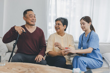 Nurse assisting her old patient at nursing home. Caregiver helping senior patient sit on sofa. Friendly female nurse talking with patient at nursing home