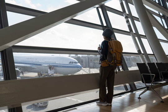 Traveler woman plan and backpack see airplane flight at the airport glass window