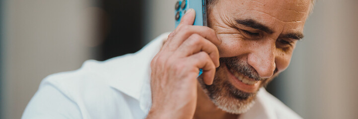 Close-up mature businessman with neat beard uses mobile phone sits on bench in the financial district in the city, Panorama. Successful man talking on smartphone.