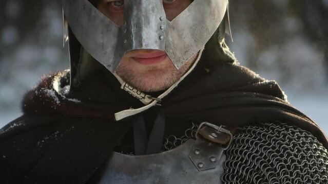 Portrait of a medieval fantasy warrior in a horned helmet, steel breastplate, chainmail with a two-handed ax in his hands, posing against the backdrop of a winter forest. Camera movement.