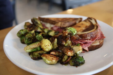 Cooked Reuben sandwich and grilled brussels sprouts on a plate in a restaurant	