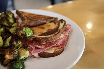 Cooked Reuben sandwich and grilled brussels sprouts on a plate in a restaurant	
