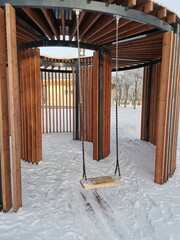 Wooden gazebo iwith swings in january park