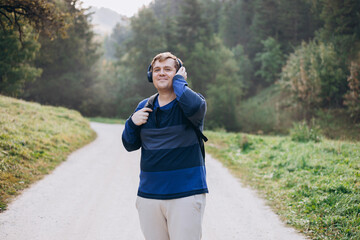 Active Young male with backpack and headphones hiking on the road in nature. 30s men walking on nature in sport clothes. Guy portrait lifestyle.