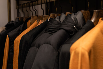 Fototapeta premium wardrobe with men's clothes in dark colors. jacket, down jacket, shirt. The clothes are neatly hung on wooden hangers