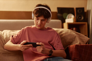 Portrait of young teenage boy playing mobile games using smartphone sitting on floor at home © Seventyfour