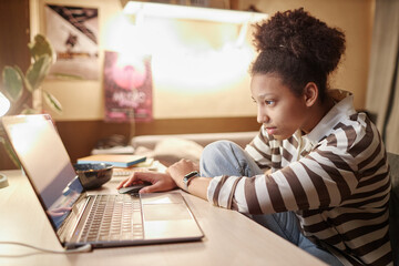 Side view portrait of teenage African American girl using laptop at night in dimly lit room