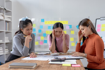 Three young asian businesswomen appear concerned while closely examining financial reports,...