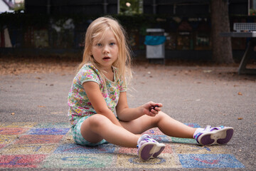 Child girl blonde preschool age is played sitting on the pavement