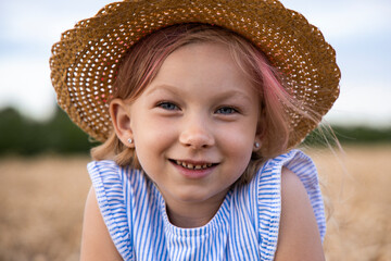 Cute child little girl in a hat on a background of a wheat field