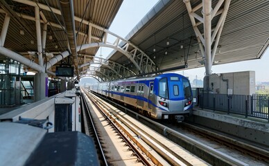 Obraz premium Scenic view of a metro train traveling on the elevated railway of Taoyuan Airport MRT System and arriving at Sports Park Station on a beautiful sunny day in Zhongli, Taoyuan City, Taiwan