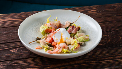 Fresh salad with egg, bacon, capers, tomatoes and lettuce on wooden table.