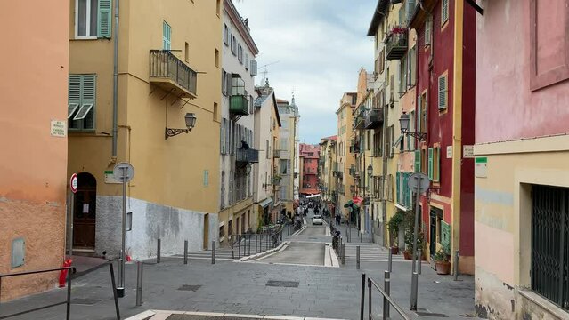 Car is moving through old narrow street at Old town of Nice. Traditional colourful houses. Pedestrians are walking. Nice, Cote d'Azur, France 