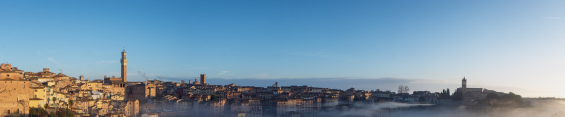 Fototapeta na wymiar Foggy sunrise in Siena, Italy, panorama with Torre del Mangia and the Church of Santa Maria dei Servi