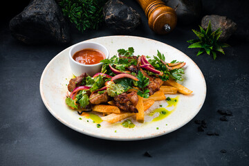 Pieces of fried pork fillet with French fries, onion, sauce and greens.