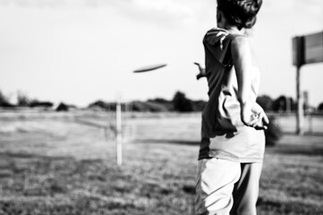 Selective focus fairway grass with a defocused young child holding a putter disc and golf goal in...
