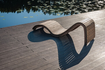 Sunbed on wooden terrace. Recreation area with sunbeds on the lake shore. - obrazy, fototapety, plakaty