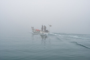 Grado, Italy - January 28th, 2024: a small fishing boat with two fishermen departs from the Mandracchio port for a fishing trip on a day of thick fog.