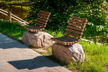 Original design infrastructure object in the city park. Wooden benches on large stones. A pedestrian path leads through the park. Smiltene Old Park, Latvia.