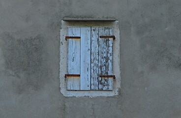 Window with closed wooden shutters on a gray gloomy plastered wall