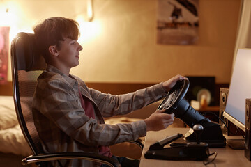 Side view of teen boy playing racing simulator video game and turning wheel, copy space