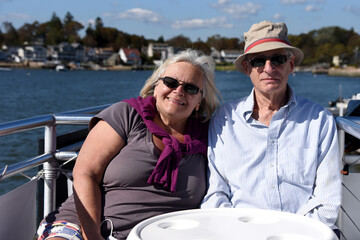 Senior couple wearing sunglasses smiling enjoying boat ride together on a sunny summer day