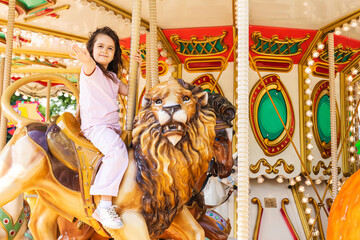 Adorable little girl in pink light clothes at amusement park having a ride on the merry-go-round