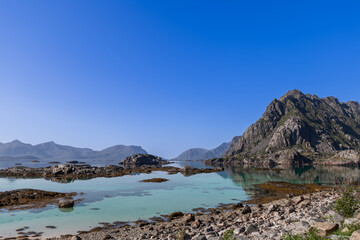 Fototapeta na wymiar A serene landscape featuring the crystal-clear waters of the Norwegian Sea and the rugged peaks of the Lofoten Islands under a clear blue sky