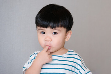 Portrait of funny baby toddler sucking finger, asian baby making funny face isolated on gray background