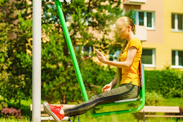 Girl doing exercises outdoor, holding phone