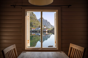 View from inside a traditional Rorbu cabin on Lofoten Islands, Norway, showcasing a mirror-like fjord and quaint fishing villages