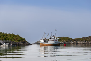 Quietude envelops a Lofoten inlet, with a solitary fishing boat anchored, reflecting on the water's...