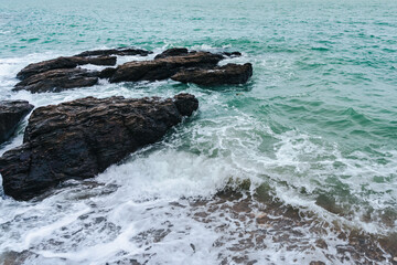 Top view of waves splashing on rock in sea shore, pretty calm sea. Landscape of rocky shores of Thai gulf with waves crashing. Seascape of east coast. Big wave in storm breaks on stones at pier.