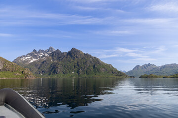The edge of a speed boat enters the frame, offering a dynamic perspective of the Lofoten fjords' mirror-like waters and jagged peaks under a wide sky