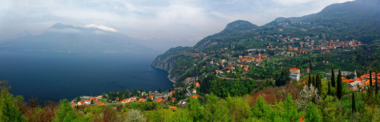 Obraz premium A panoramic view from Vezio Castle on the mountainside overlooking beautiful Lake Como with villages on lakeside hills and snow capped alpine mountains in background on a cloudy day, in Varenna, Italy