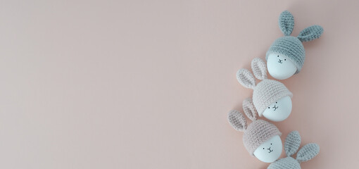 Minimalistic Easter background, banner. Bunnies in knitted hats on a pink background.