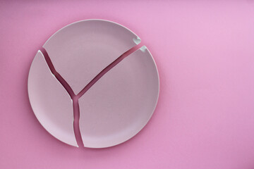 A broken pink ceramic plate on a gray background. view from above. The concept of diet, old things
