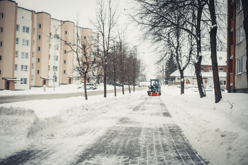 The tractor clears the road from snow. Blown snow on the city path. 