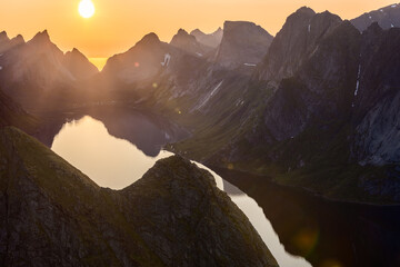 The midnight sun casts a hazy glow over Reinebringen, with steep peaks framing the still waters...