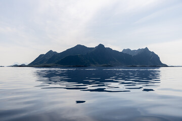 A serene panorama of the Lofoten Islands, with glassy waters reflecting the jagged peaks under a...