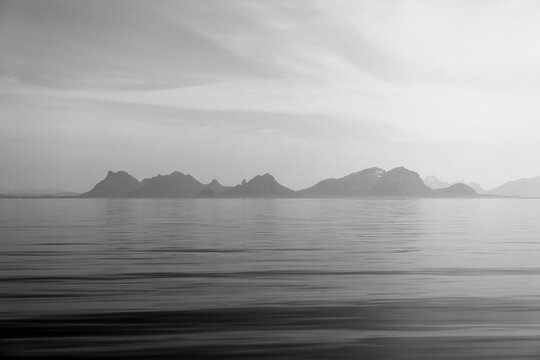 Monochrome image capturing the peaceful silhouette of Lofoten mountains against a soft-lit sky, reflected in the still Norwegian waters