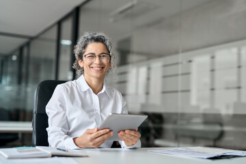 Happy middle aged professional business woman using tab computer in office. Mature female bank...